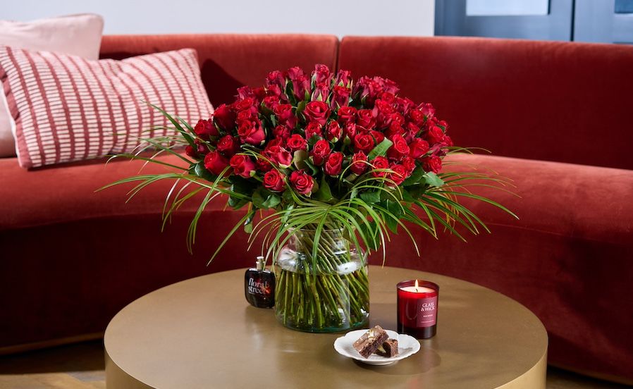 A large bouquet of red roses with a candle, perfume and brownies
