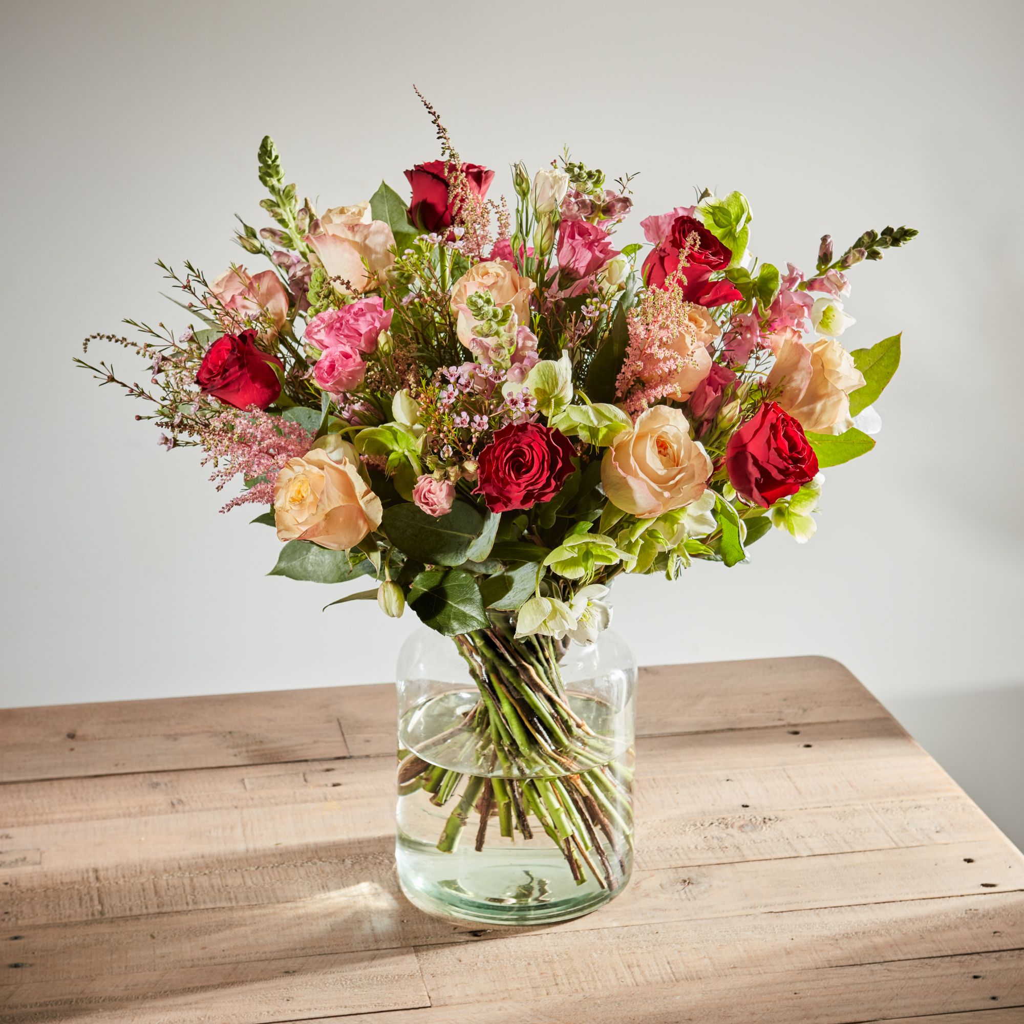 Red Rhodos roses, Victorian Peach roses, dark pink lisianthus, dark pink astilbe, pink waxflower, lavender antirrhinums, white hellebores and eucalyptus cinerea.