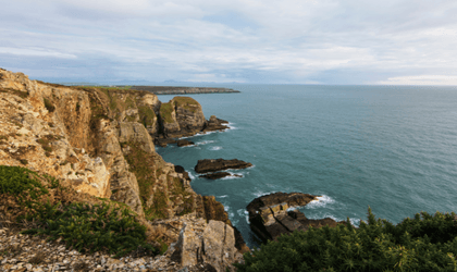 Photograph of coastal cliffs looking out over a deep green/blue sea.