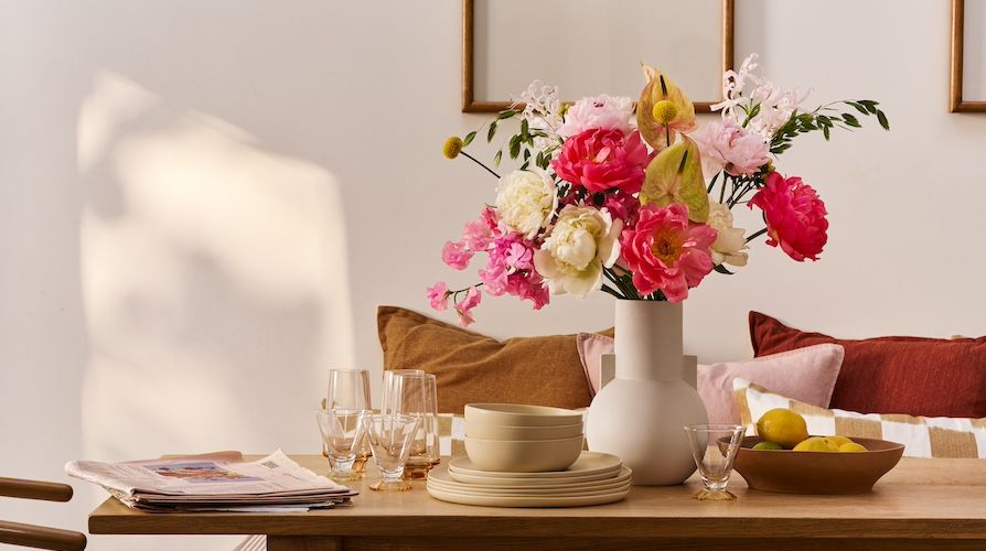 A bouquet of white and pink peonies on a dining table with crockery and glassware