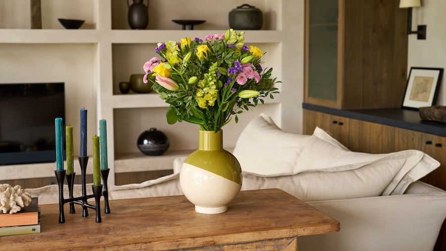 A bouquet of lilies, roses and antirrhinum sit on a sideboard in a neutral living room