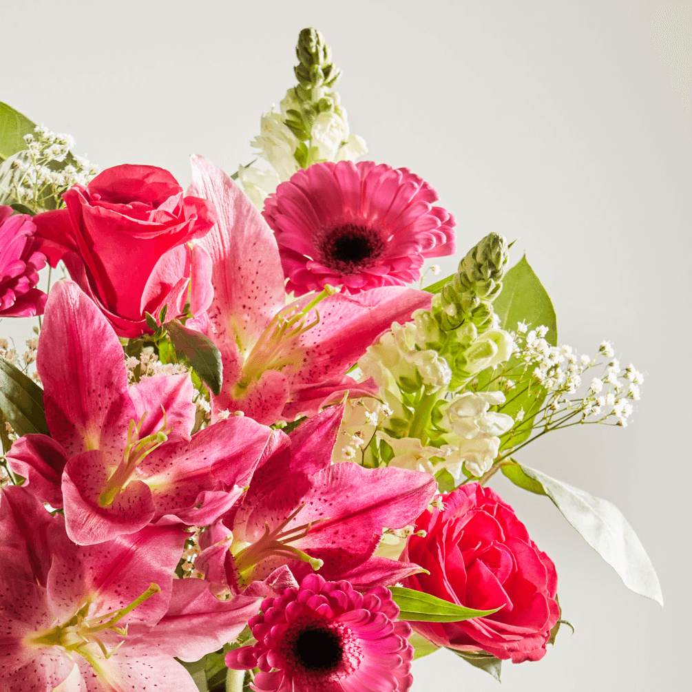 Close up photo of a vibrant bouquet of pink flowers including lilies, gerberas and roses.