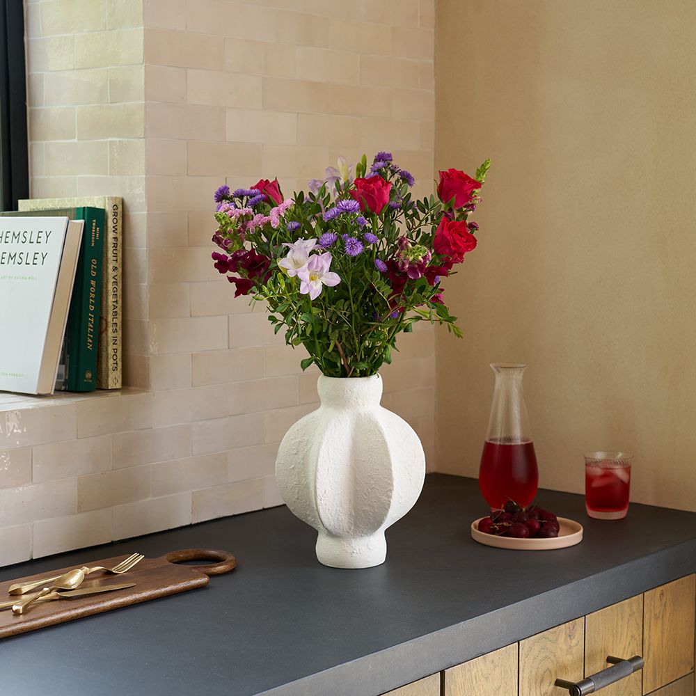 A letterbox selection of red, pink and purple flowers in a white vase