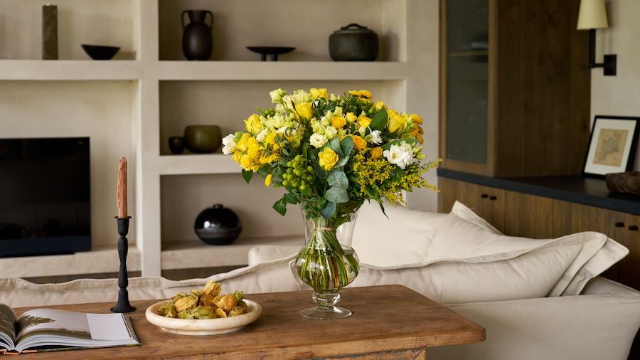 A yellow and white bouquet of flowers on a wooden sideboard