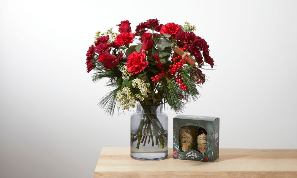 A bouquet of red carnations, roses, chrysanthemums, and ivy berries with white waxflower and green pine and eucalyptus