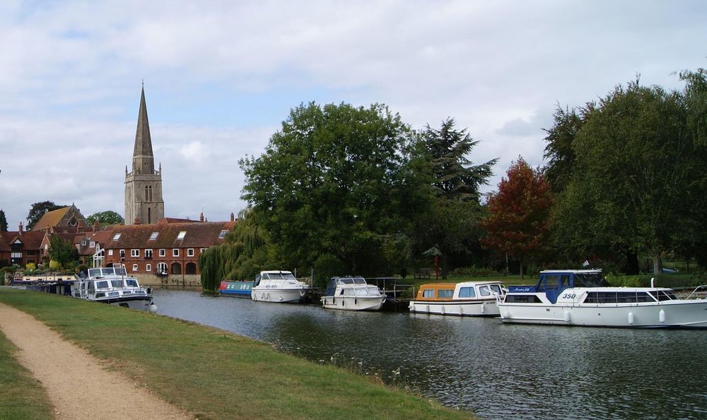 A picturesque river town viewed from the opposite bank, with boats moored on the water and a church in the distance.