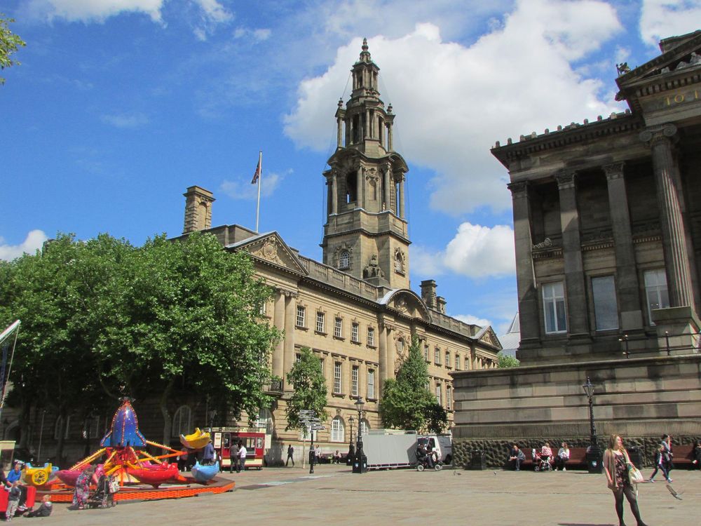 Photo of a city centre with two large stone buildings in the background, one with tall columns, the other with a tall spire.